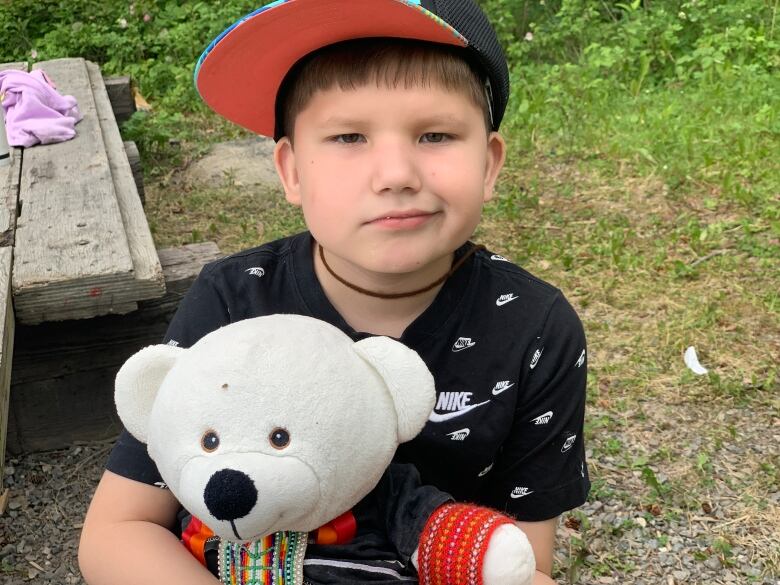 A child wearing a baseball cap holds a white bear.