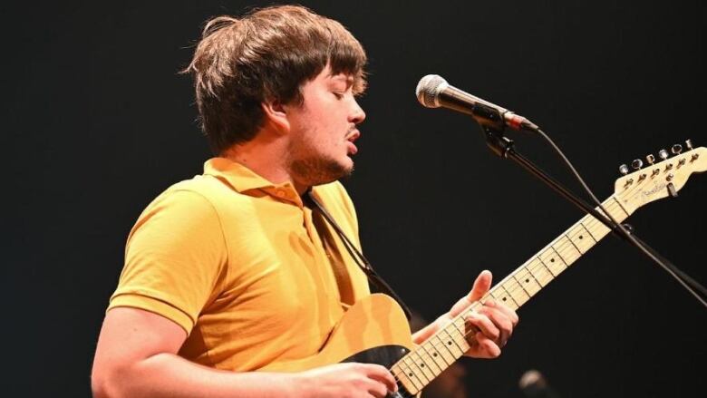 Young man, profile shot, playing guitar singing into mic.