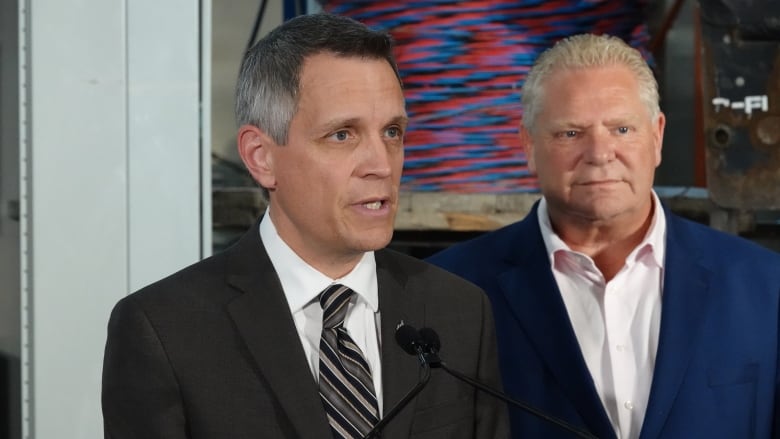 A mayor speaks into a microphone as a provincial leader stands behind him.