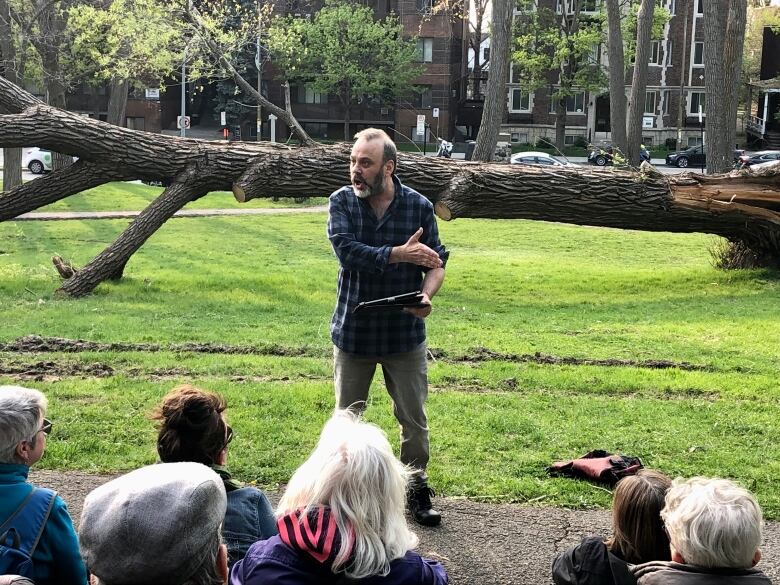 A man stands in front of a crowd in a park.