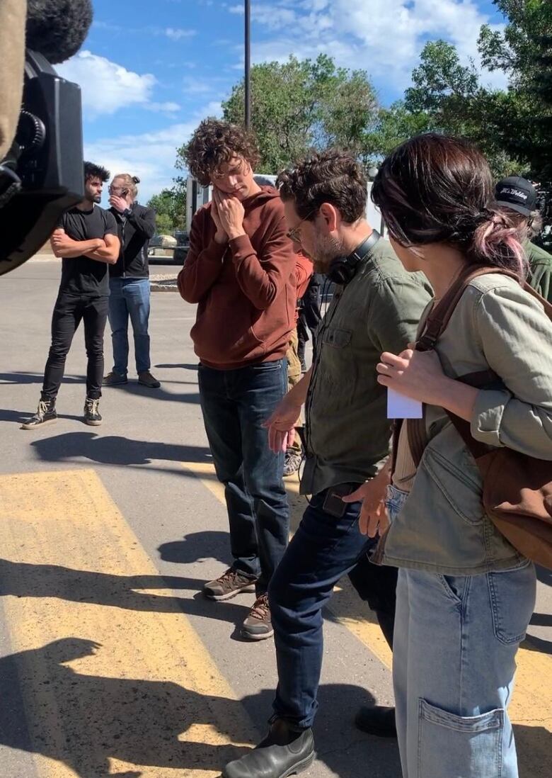 A director stands between a female and male actress on set walking them through a scene. 