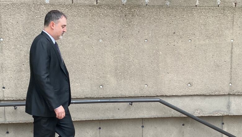 A man in a suit walks down a flight of stairs outside.