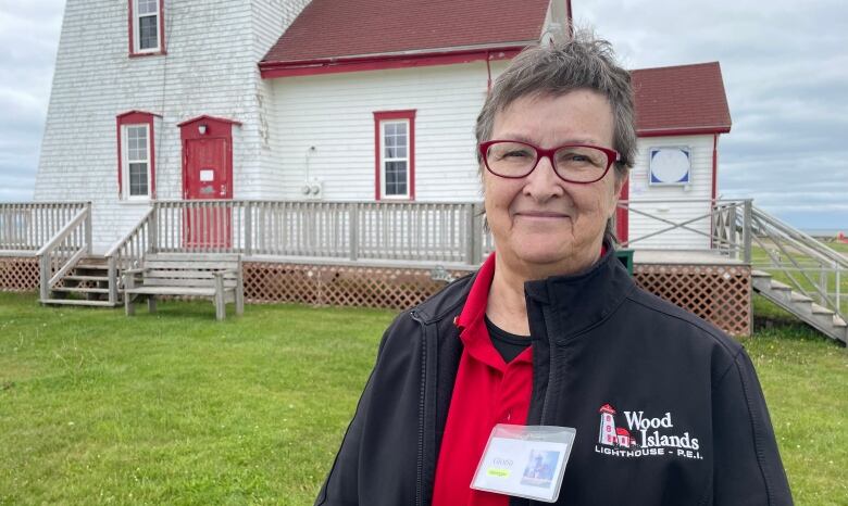 A woman stands outside a white and red lighthouse.