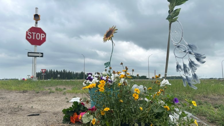 A bouquet of flowers and a dream catcher near a stop sign along the road. 