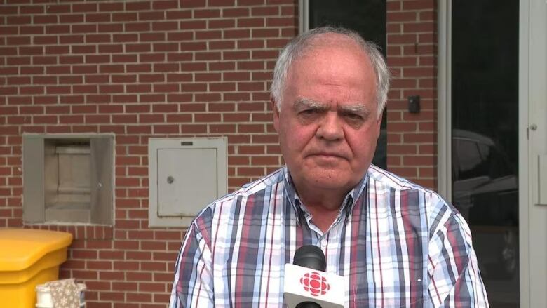 A man in a plaid shirt speaks into a CBC microphone outside a building.