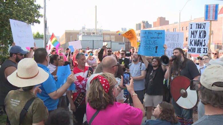 Dozens of people are on a street holding posters and pride flags. 