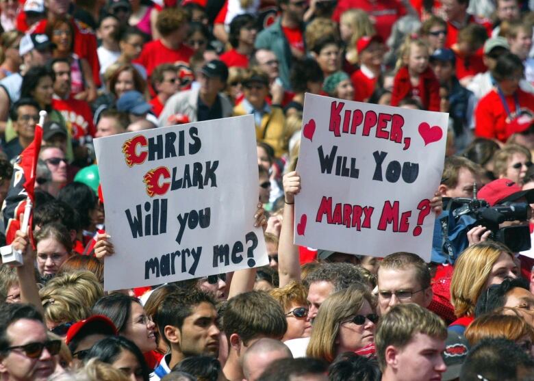 A large group of hockey fans are pictured. Two of them are holding signs.