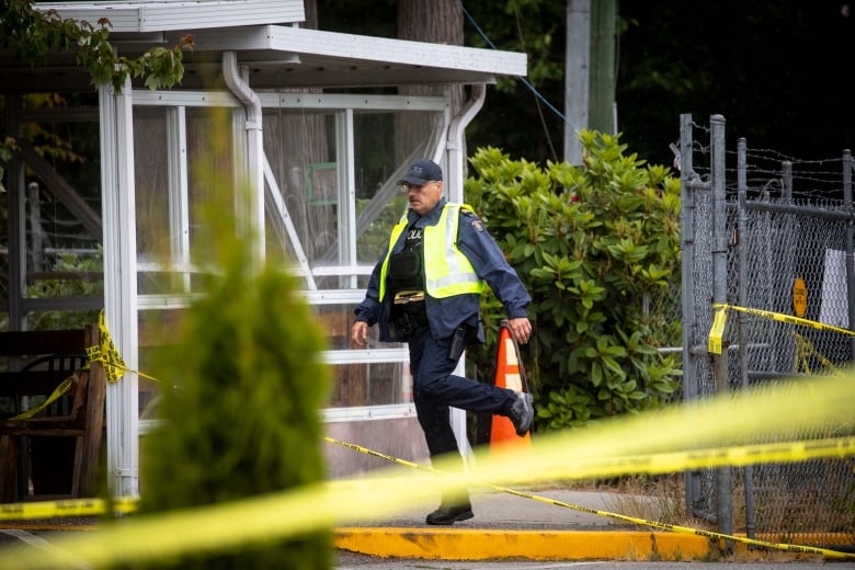 An RCMP officer walks behind yellow crime scene tape.