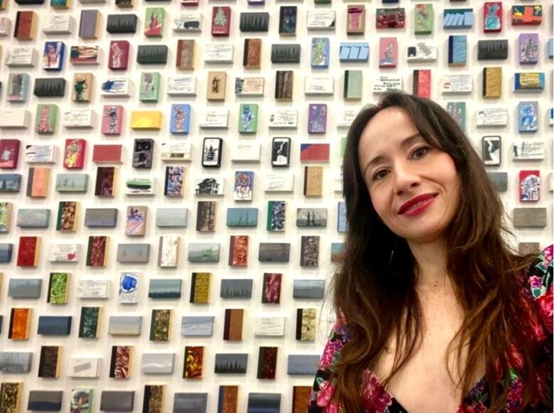 A young woman stands in front of a wall of small artwork.