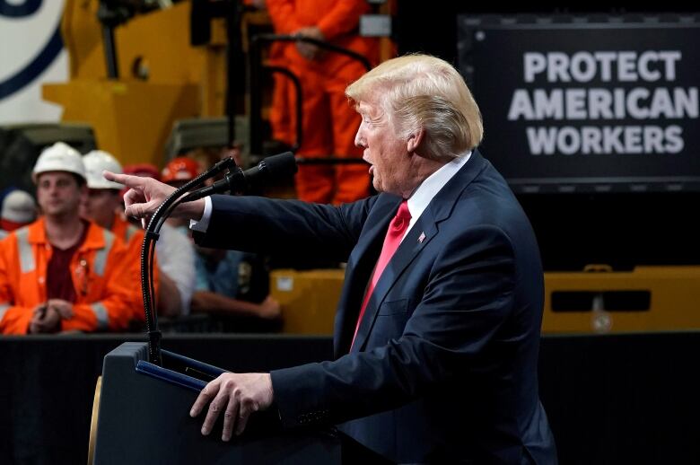 People in hardhats in background as Trump points from podium