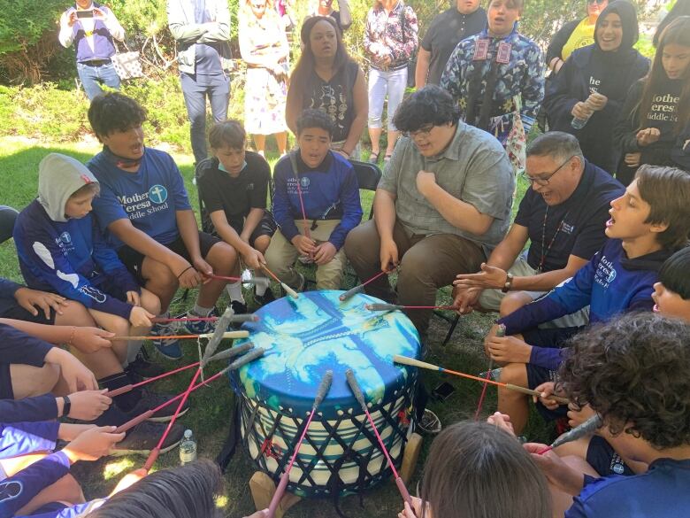 A group of boys in blue shirts sit in a drumming circle around a drum with a blue top.