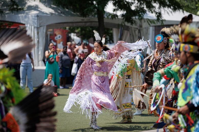 A woman in traditional Indigenous clothing dances amidst other dancers. 