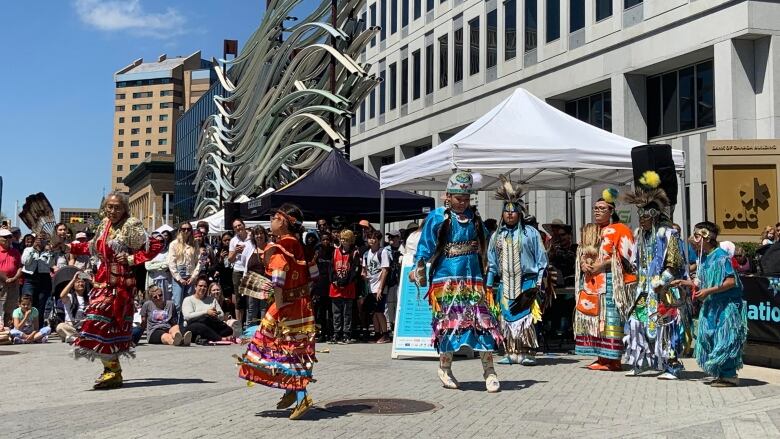 A dancer in red, a dancer in orange and a dancer in blue can be seen on a street.