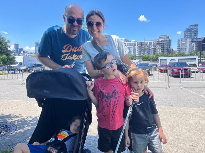 A young couple with three young children, including a boy with a Spider Man shirt with a white walking cane, smile at the camera.