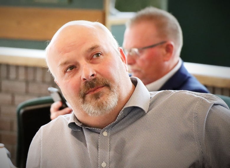 A man with a beard and moustache and grey shirt looks up at someone off camera.