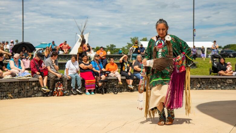 A woman dances in an outdoor powwow demonstration as people look on.