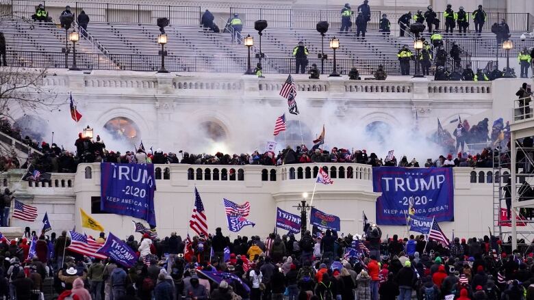 A wide shot is shown of hundreds of people gathered in a protest, with smoke rising in the air and flags held by some.