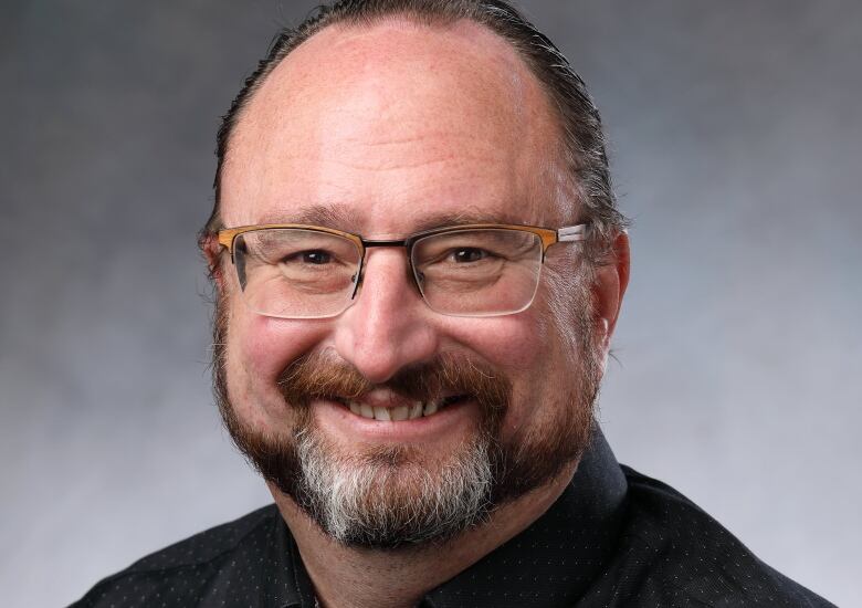 A man in a black shirt and glasses smiles