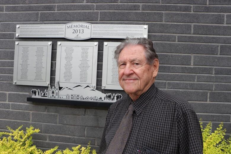 A man stands in front of a plaque listing people's names 