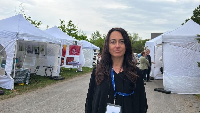 A woman stands outdoors amid several large white tents. 