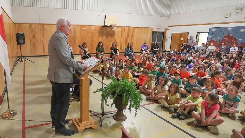 A man stands in a room with a lot of little kids.