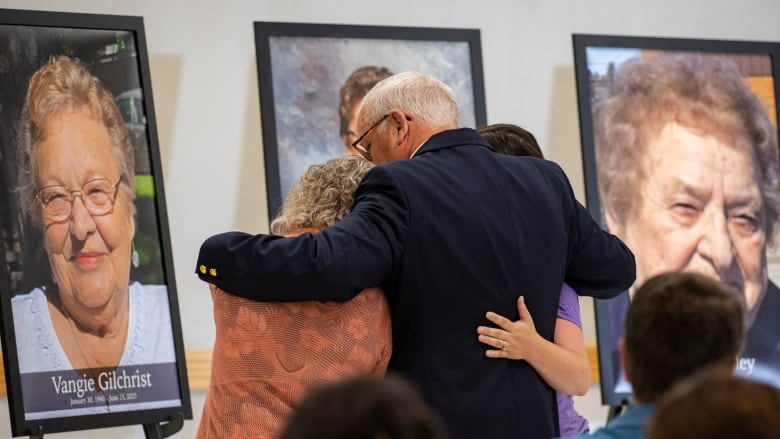 Three people embrace while looking at a large photo of their loved one. 