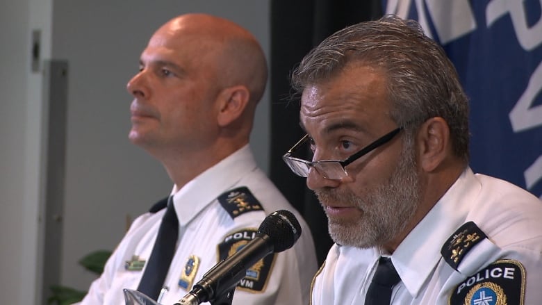 Two men in police uniforms speak to media.