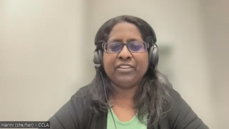 A woman sits with a blurred background and headphones on.