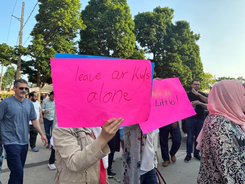 People holding up pink signs that read, 'Leave Our Kids Alone.' 