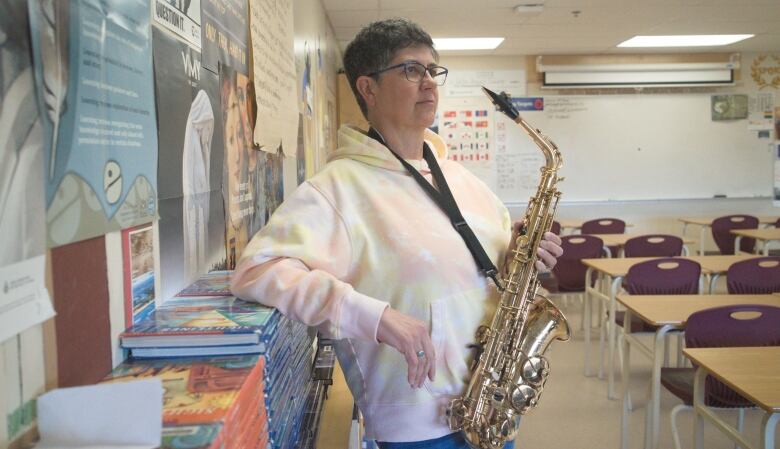 woman holding saxophone inside a classroom looking off camera