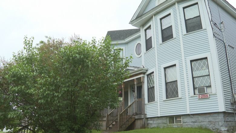 Two story blue and white house with a large bush in front.