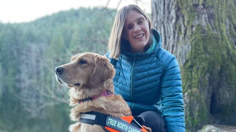 A woman wearing a blue jacket kneeling next to a golden retriever dog.