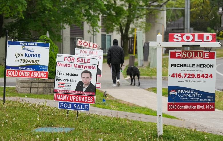 A person walks past multiple for-sale and sold real estate signs in Mississauga, Ont.