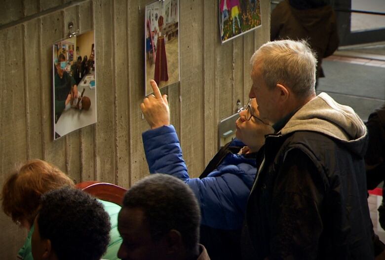 A group of people looking at photographs on a wall. 