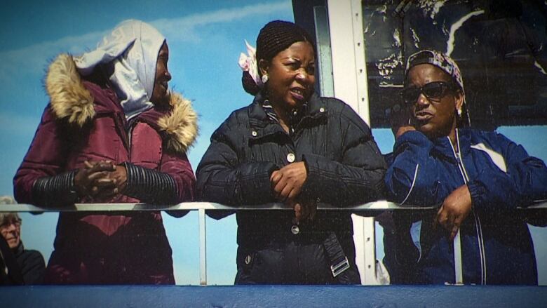 Three women stand next to the rail on a ship. 