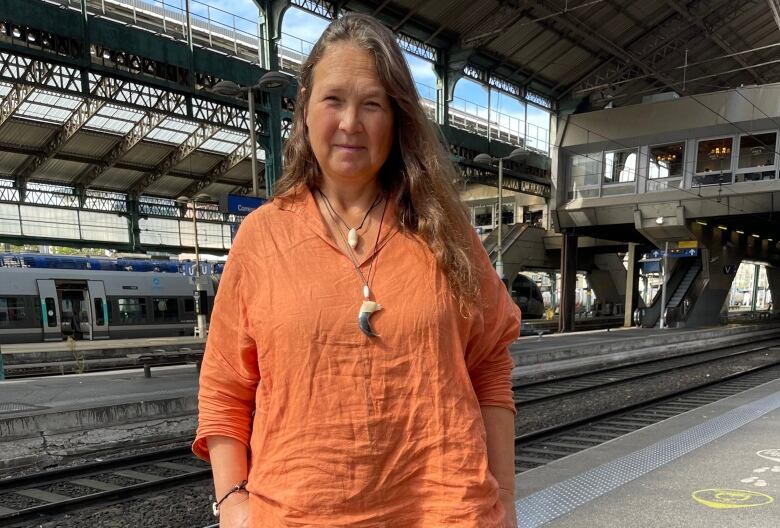 A woman with long brownish hair wears an orange shirt.