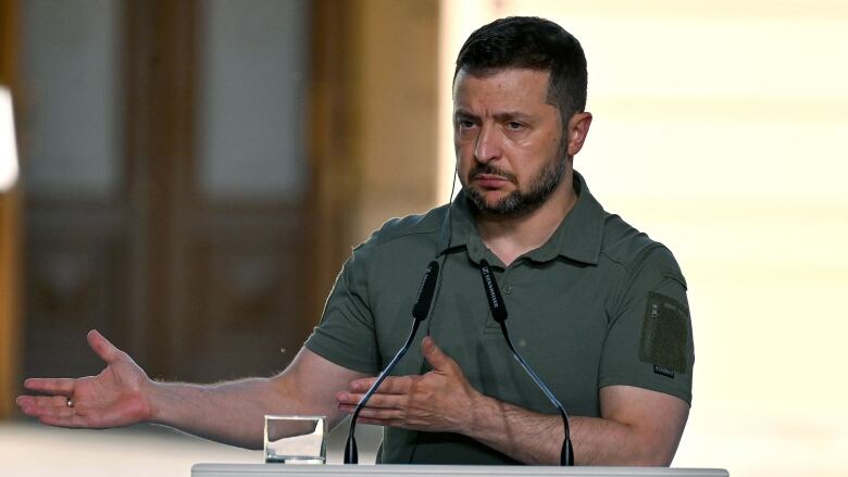 A person gestures while speaking at a lectern featuring the Ukraine flag.