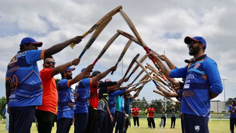 Players touch their cricket paddles in the air creating a tunnel for others to walk under. 