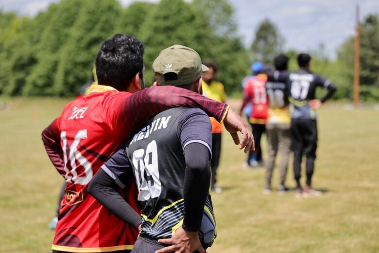 One cricket player has his arm around another as they watch play. 