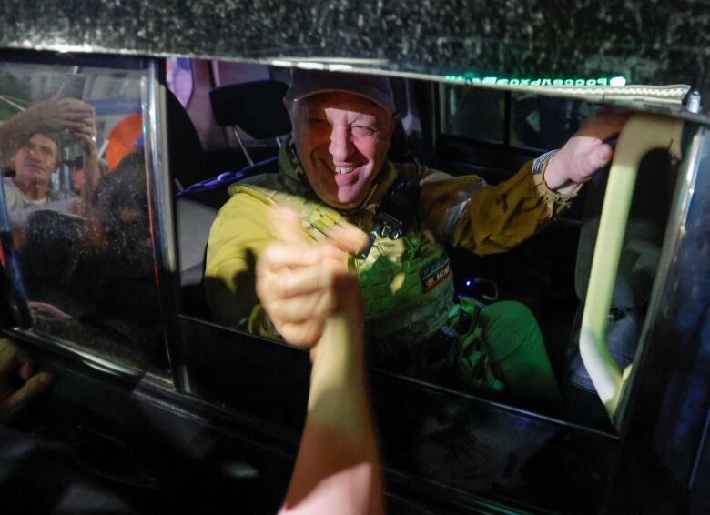 A man smiles as he shakes a hand through a car window.