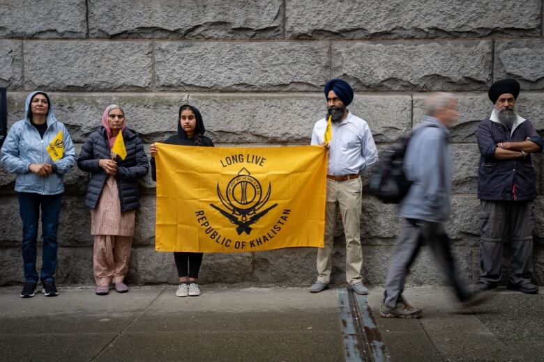 People are pictured lined against a wall, holding a yellow flag that reads, 