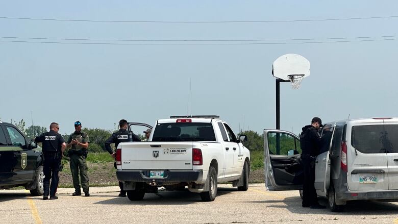 Uniformed men gather around a number of trucks in a parking lot on a sunny day. 