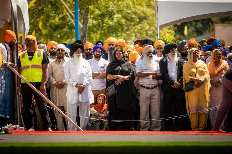 A woman sits on the ground surrounded by a crowd of Sikh mourners at a funeral.