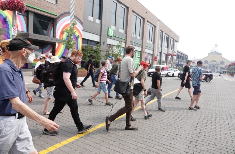 A group of people follow a city councillor across a street on a tour.