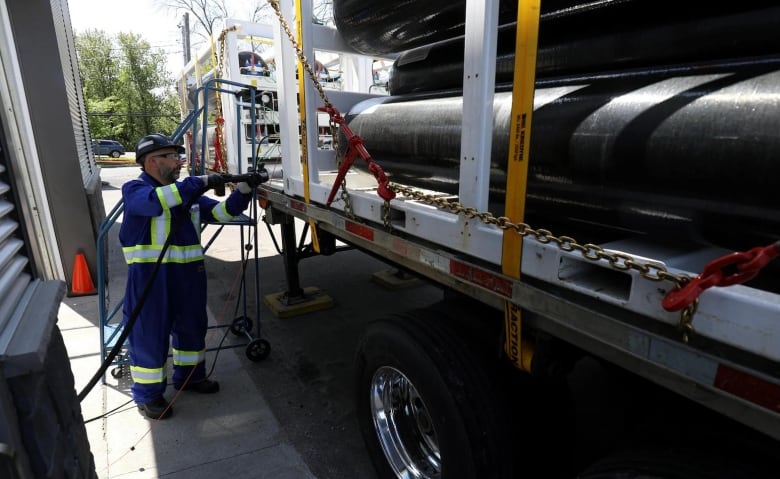 A man works beside a flatbed truck with many black cylinders sitting on it.