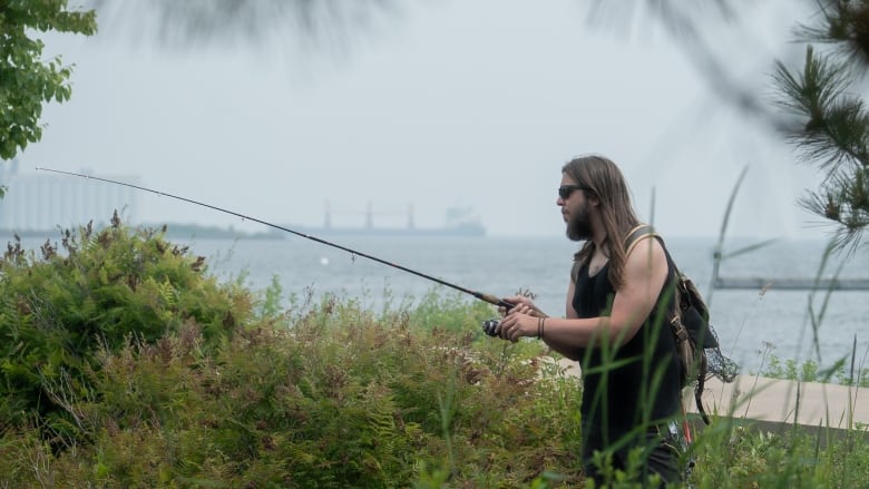 A man wearing sunglasses and a tank top holds a fishing rod.