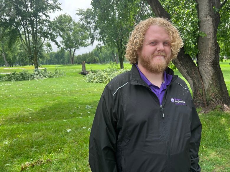 A man in a black windbreaker in front of a tree.