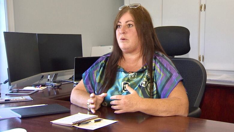 A woman sits behind a desk while speaking to the camera.