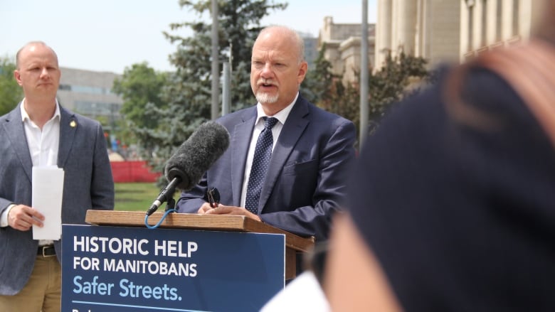 A politician speaks into a microphone at a podium outside at a government news conference.