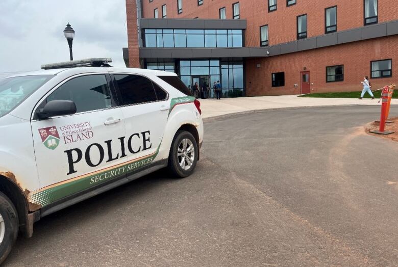 Security car stands outside a tall building with about a dozen people seen entering the building's doors behind it. 